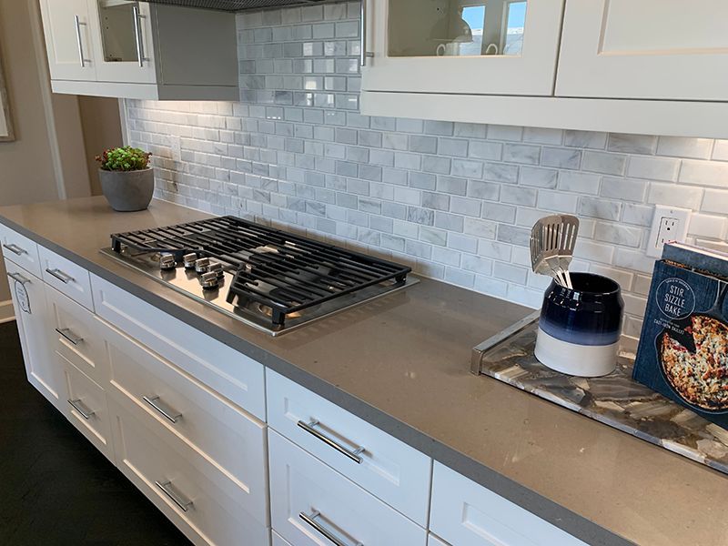 Modern kitchen countertop with a gas cooktop, white cabinets, and mosaic tile backsplash