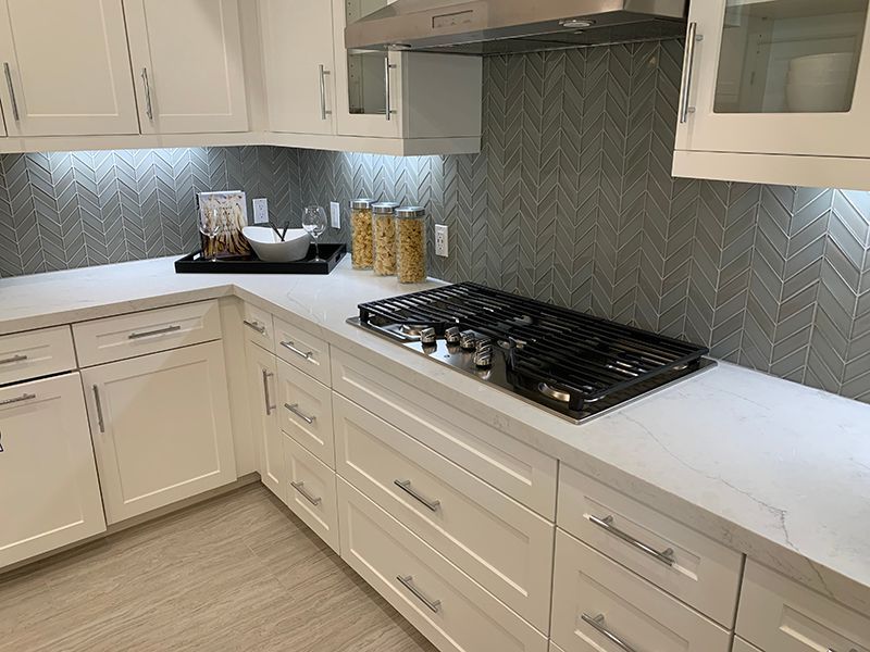 Modern white kitchen with gray backsplash, white cabinets, marble-look counters, and black gas cooktop.