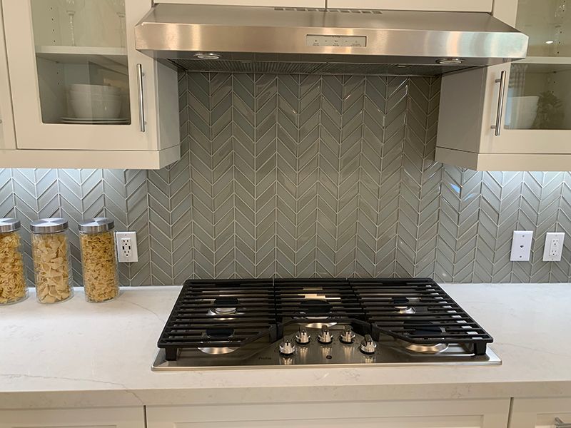 Modern kitchen with stainless steel range hood, gas cooktop, and herringbone tile backsplash