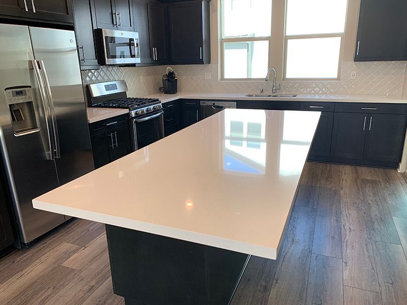 Modern kitchen with white island, dark cabinets, stainless appliances, and wood-look flooring