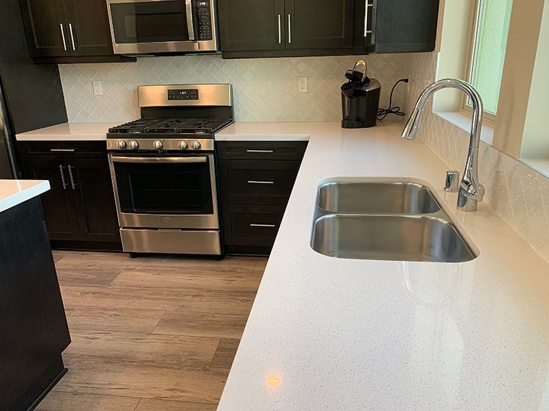 Modern kitchen with dark cabinets, stainless steel stove, and white countertop with double sink.