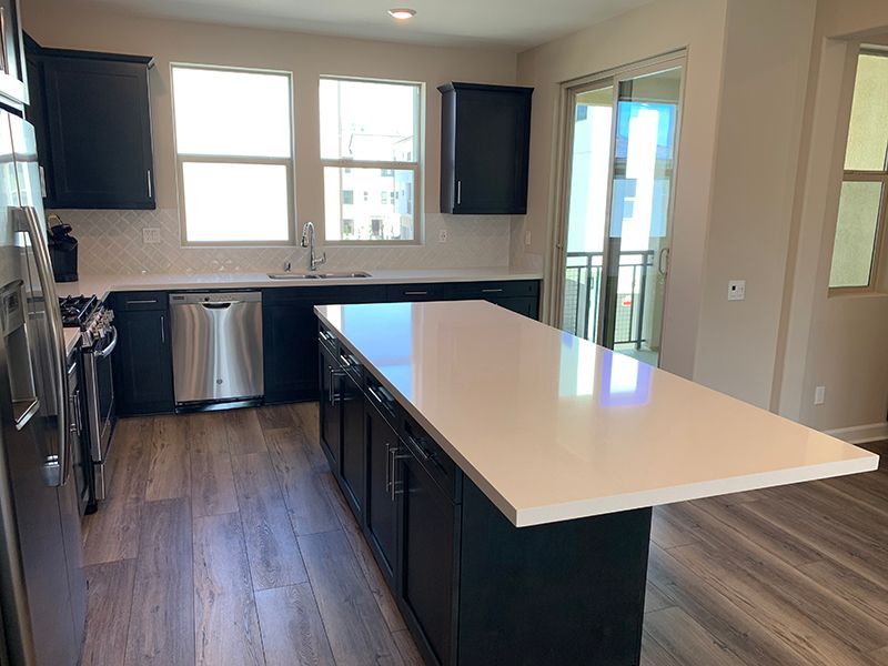 Modern kitchen with dark cabinets, white island countertop, stainless appliances, and wood floors.