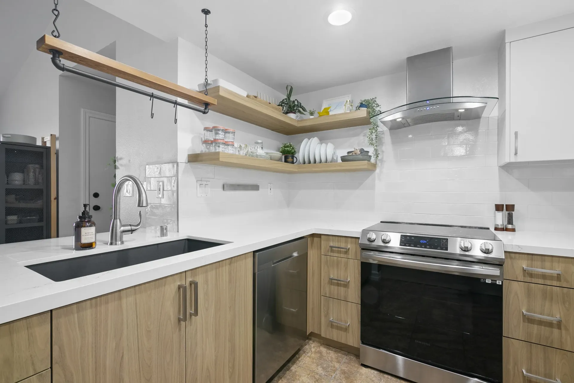 Bright modern kitchen with white cabinets, wood shelves, black stove, and farmhouse sink