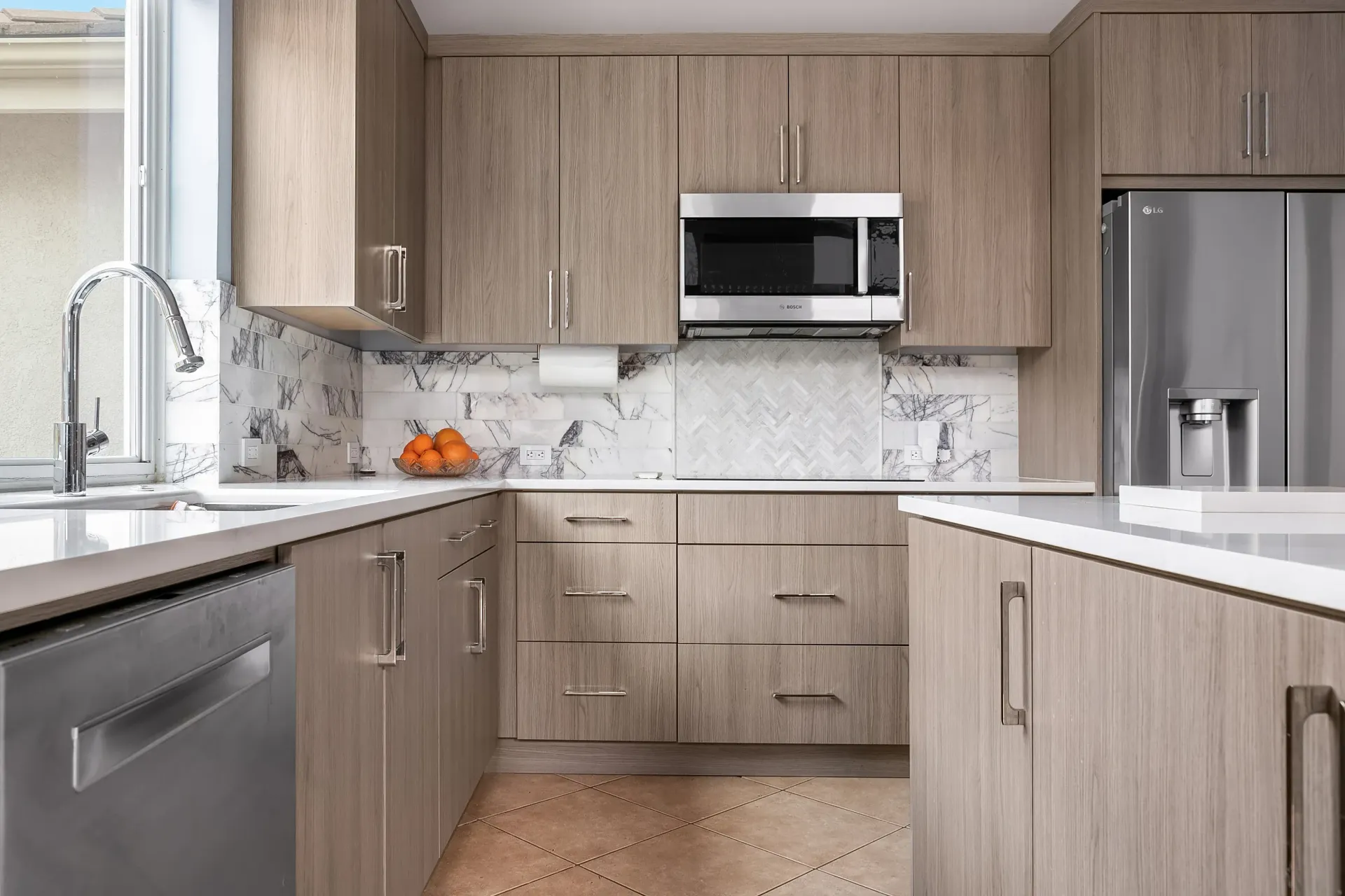 Modern kitchen with light wood cabinets, stainless steel appliances, white countertops, and marble backsplash.