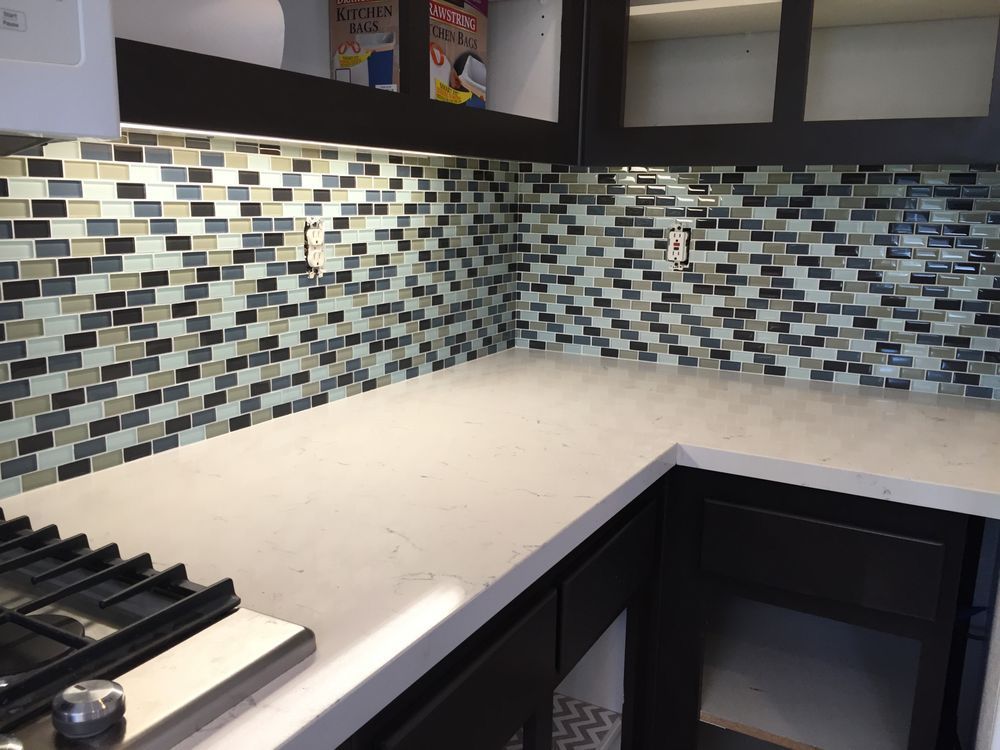 Modern kitchen with dark cabinets, gas stove, white countertop, and blue-gray mosaic tile backsplash