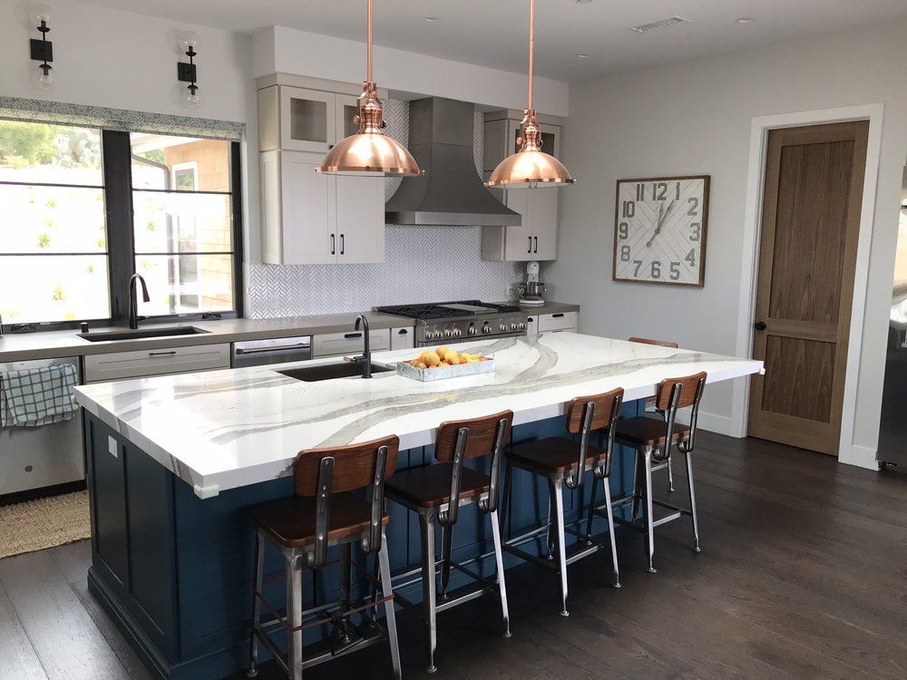 Modern kitchen with white island, dark stools, pendant lights, and wood floors