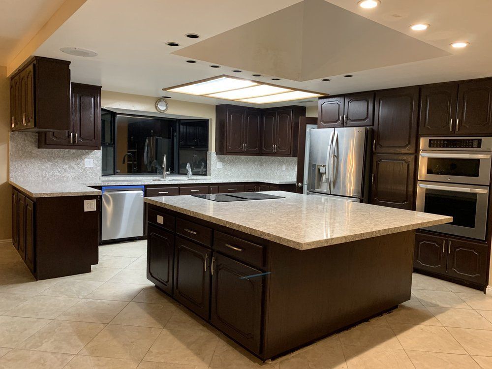 Modern kitchen with dark wood cabinets, stainless steel appliances, and a large island with a light countertop