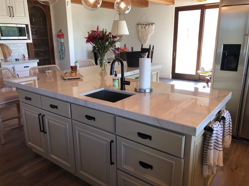 Modern kitchen with a gray island, white countertop, sink, flowers, and sunlight by large windows