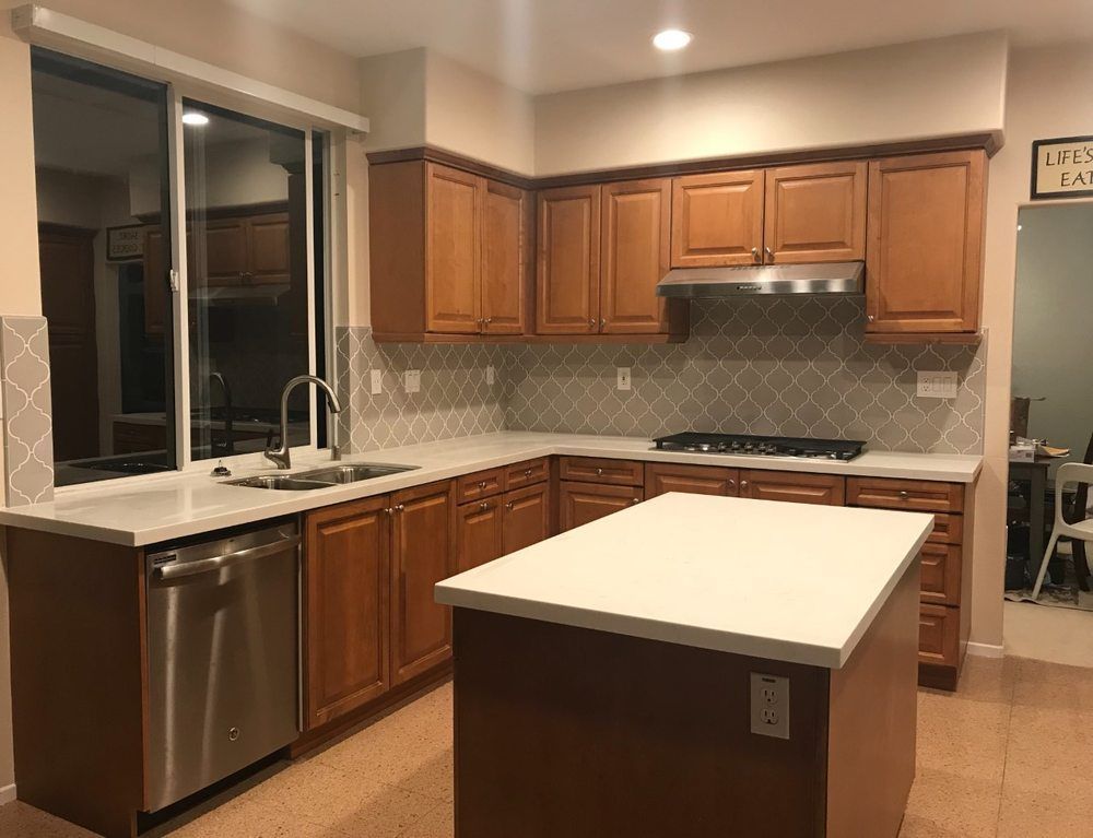 Modern kitchen with dark wood cabinets, stainless appliances, white countertops, and a central island.