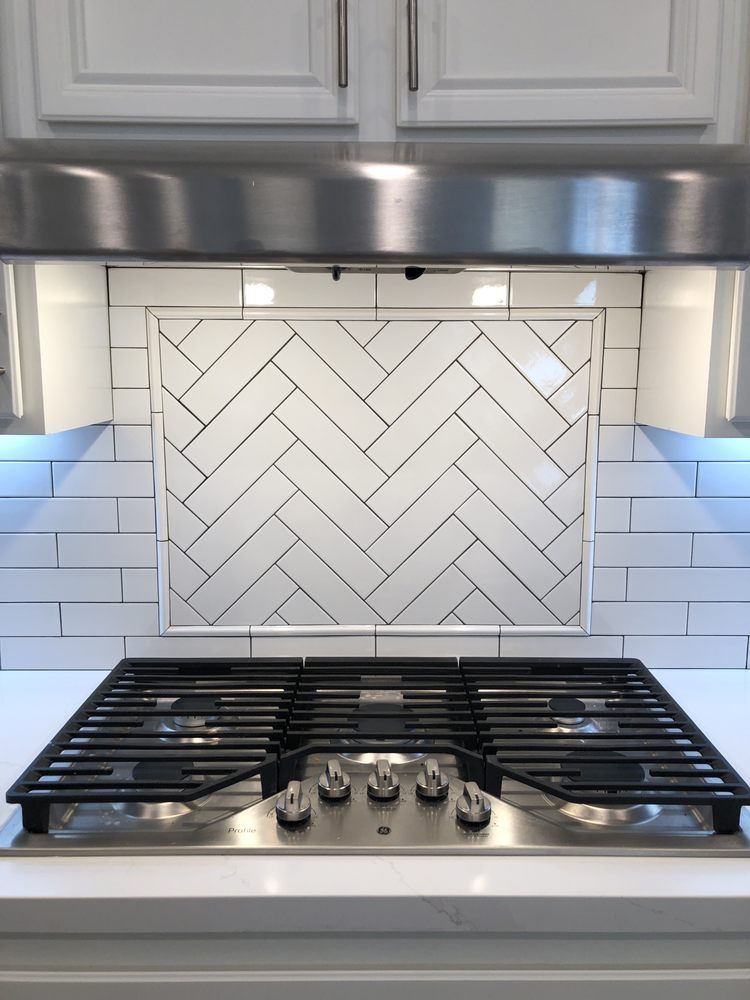 Modern kitchen stove with stainless hood and white herringbone tile backsplash