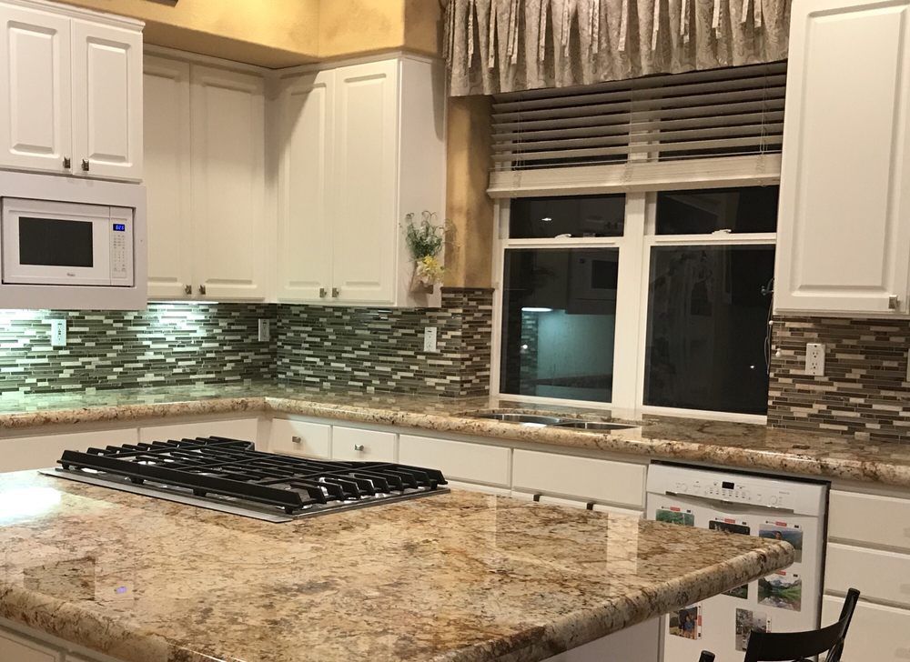 Modern kitchen with white cabinets, granite island, gas cooktop, and window above the sink