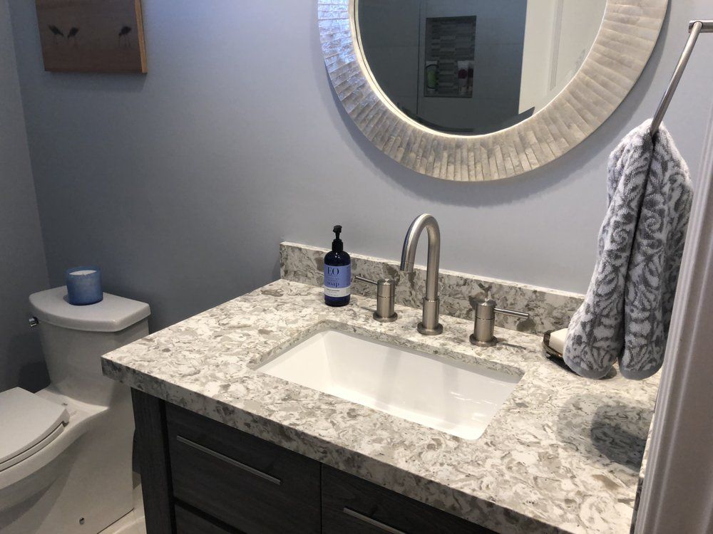 Small bathroom vanity with granite countertop, sink, round mirror, soap dispenser, and hand towel