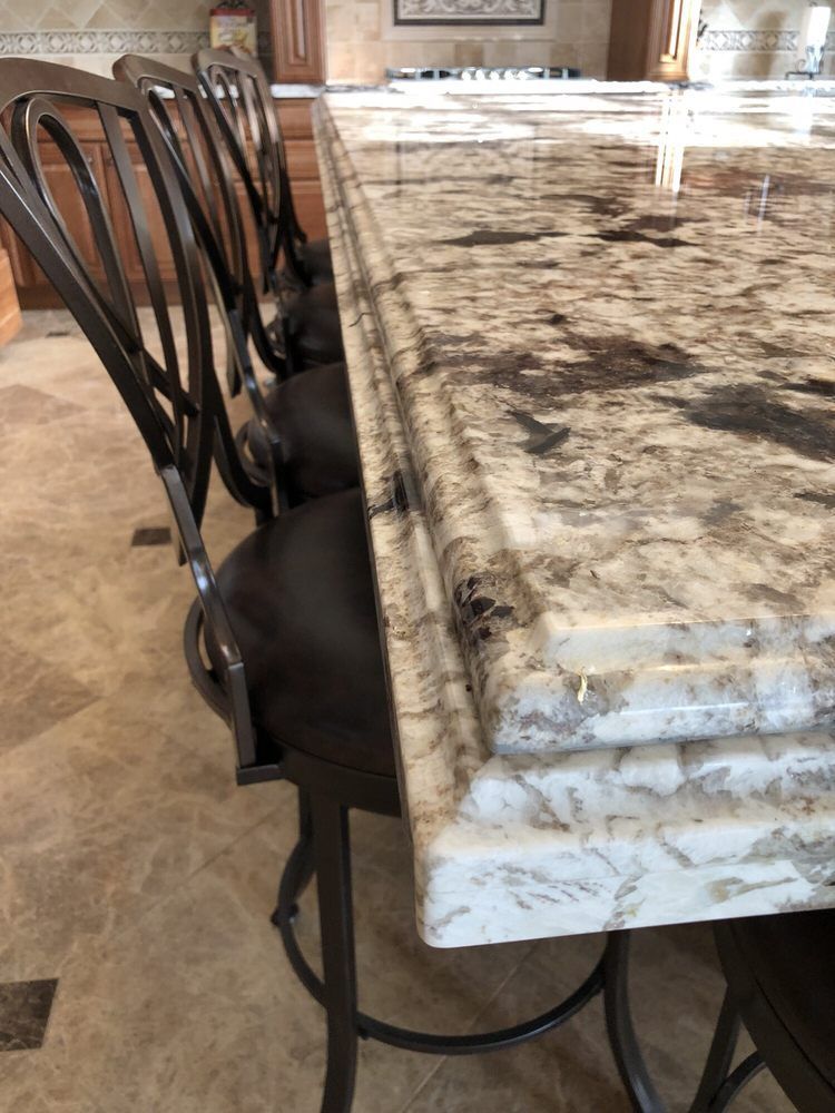 Black dining chairs beside a long marble kitchen island in a bright room