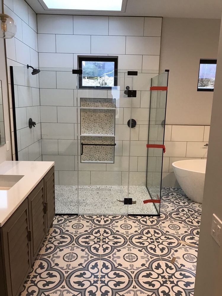 Modern bathroom with glass shower, patterned floor tiles, vanity, and toilet.