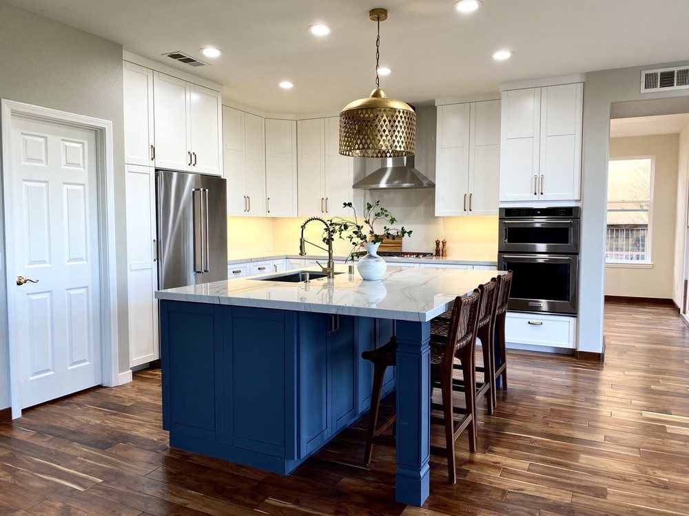 Modern kitchen with navy island, white cabinets, stainless fridge, and wood floors.