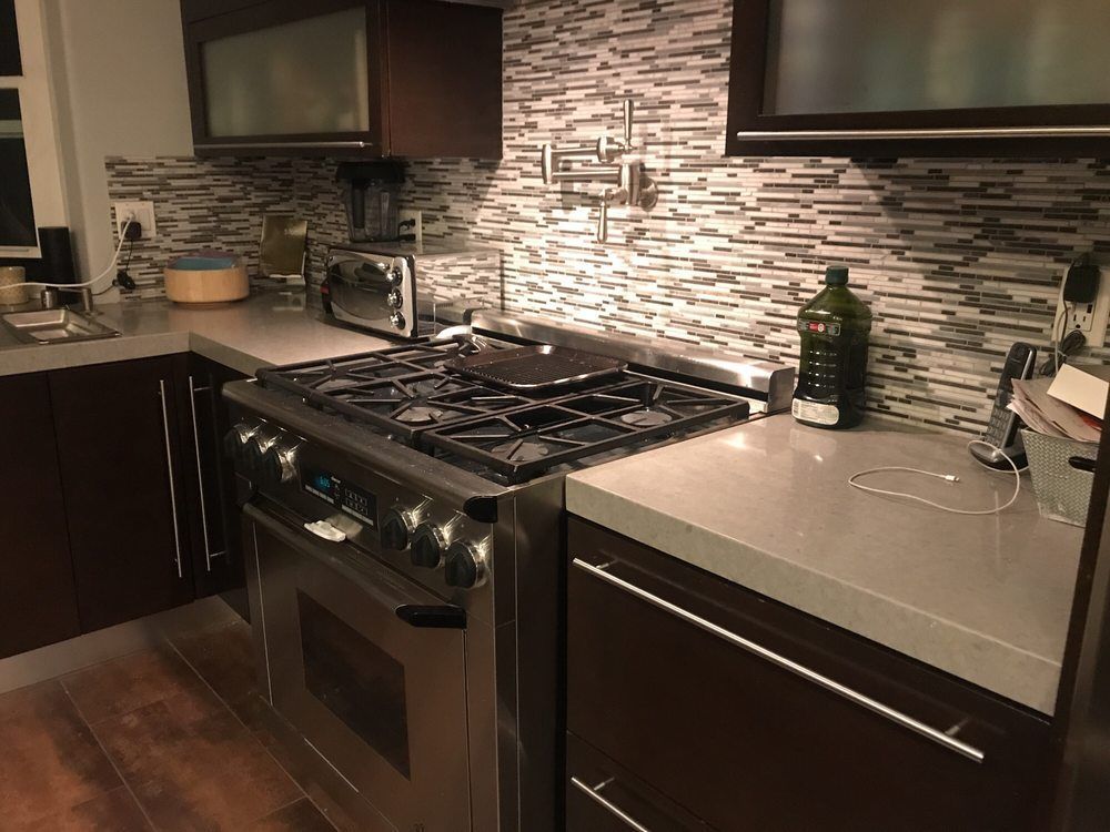 Modern kitchen with dark cabinets, stainless steel stove, and mosaic tile backsplash