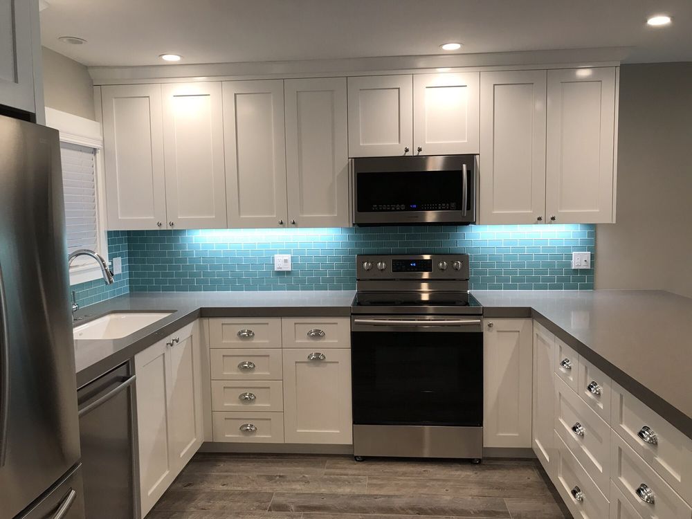 Modern white kitchen with stainless steel appliances and blue tile backsplash