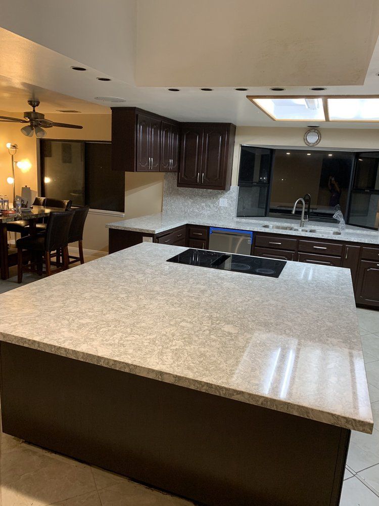 Modern kitchen with large island, dark cabinets, and stainless steel sink under recessed lighting
