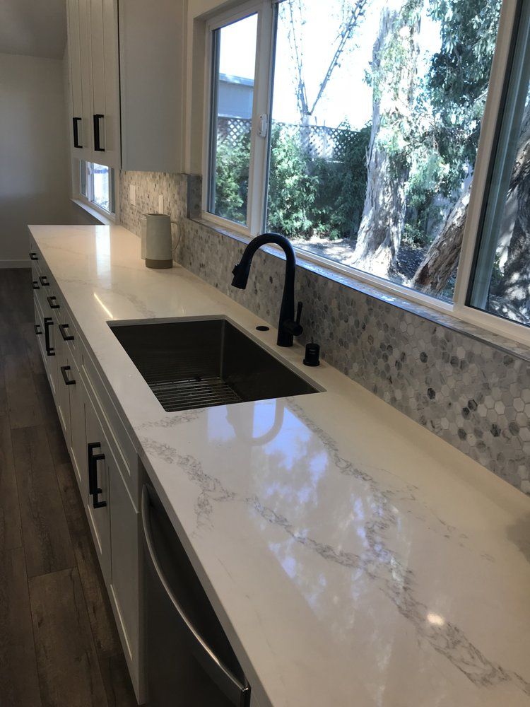 Modern kitchen countertop with sink, black faucet, white cabinets, and large window overlooking greenery