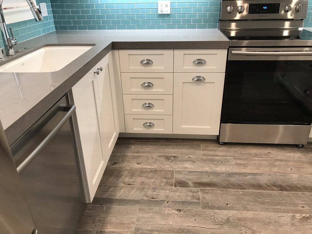 Modern kitchen with white cabinets, teal tile backsplash, black stove, and wood-look floor