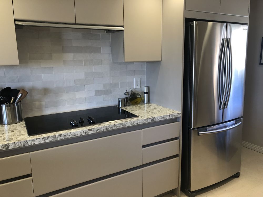 Modern kitchen with beige cabinets, granite counters, stainless steel refrigerator, and sink under a tiled backsplash