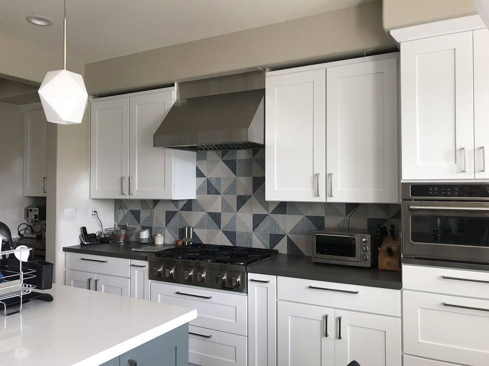 Modern kitchen with white cabinets, black countertops, stainless range hood, and gray geometric tile backsplash
