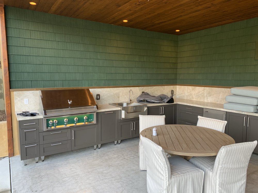 Outdoor patio with grill, cabinets, and round table with white chairs against green wall.