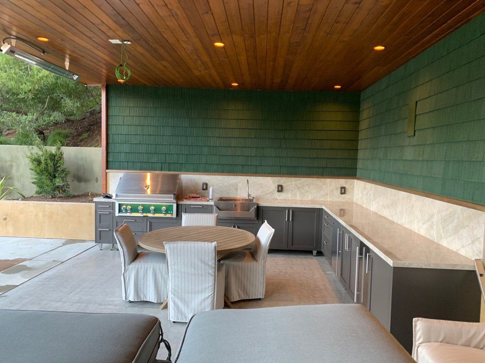Covered patio with wooden ceiling, green tiled walls, grill, and a dining table with chairs