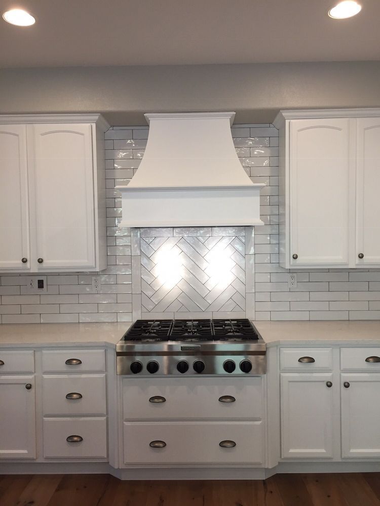 White kitchen with center stove, herringbone tile backsplash, and matching cabinets and range hood