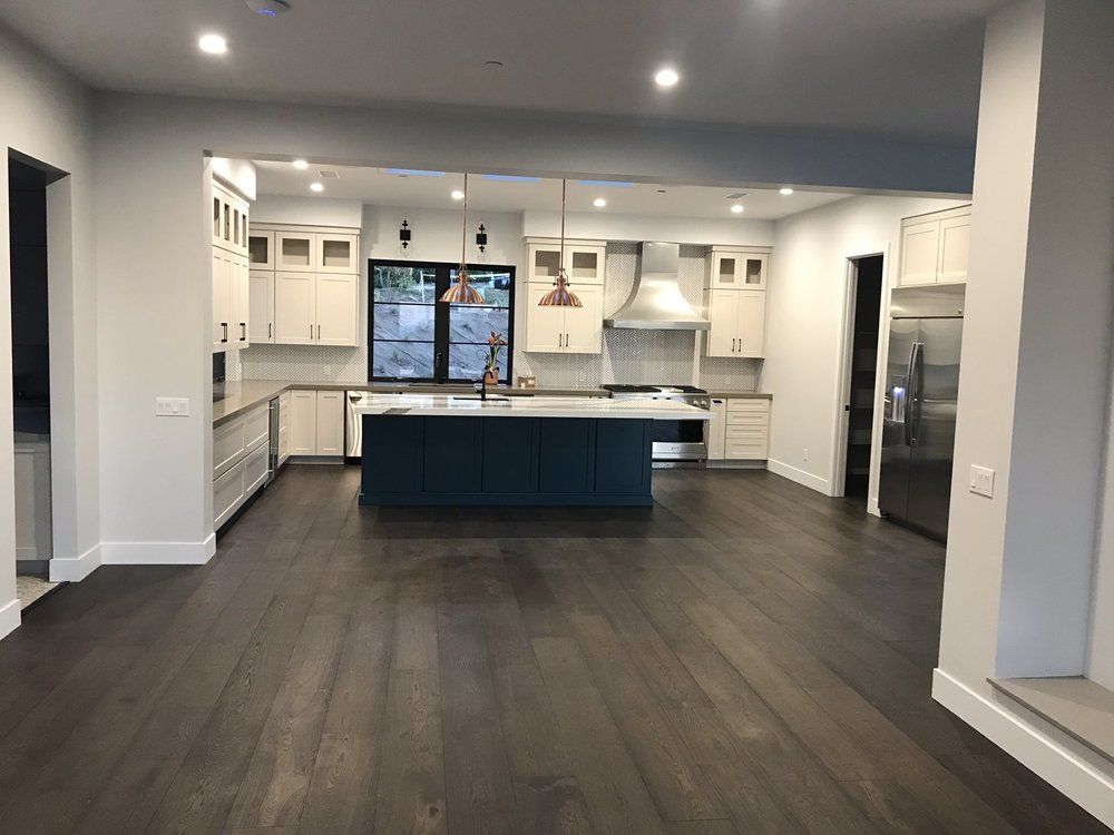 Empty modern kitchen and living area with dark floors, white cabinets, and a blue island