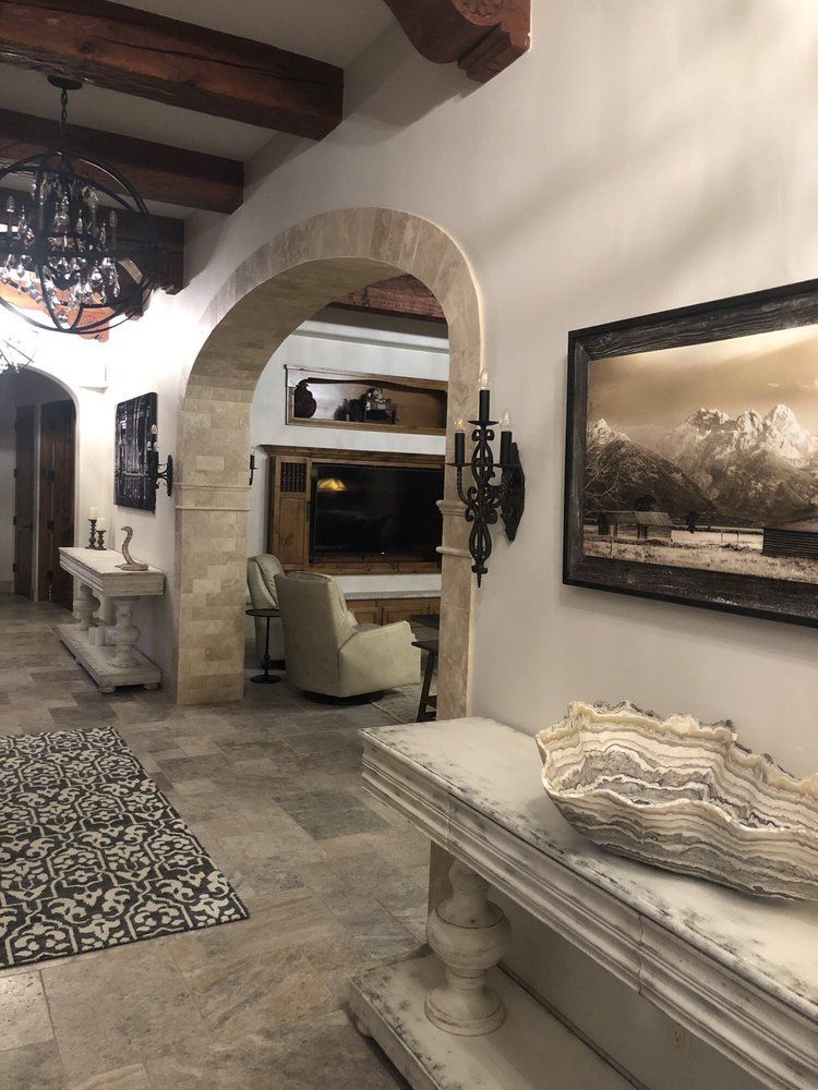Elegant stone hallway with arched doorway, rustic beams, and upholstered bench in a Mediterranean-style interior