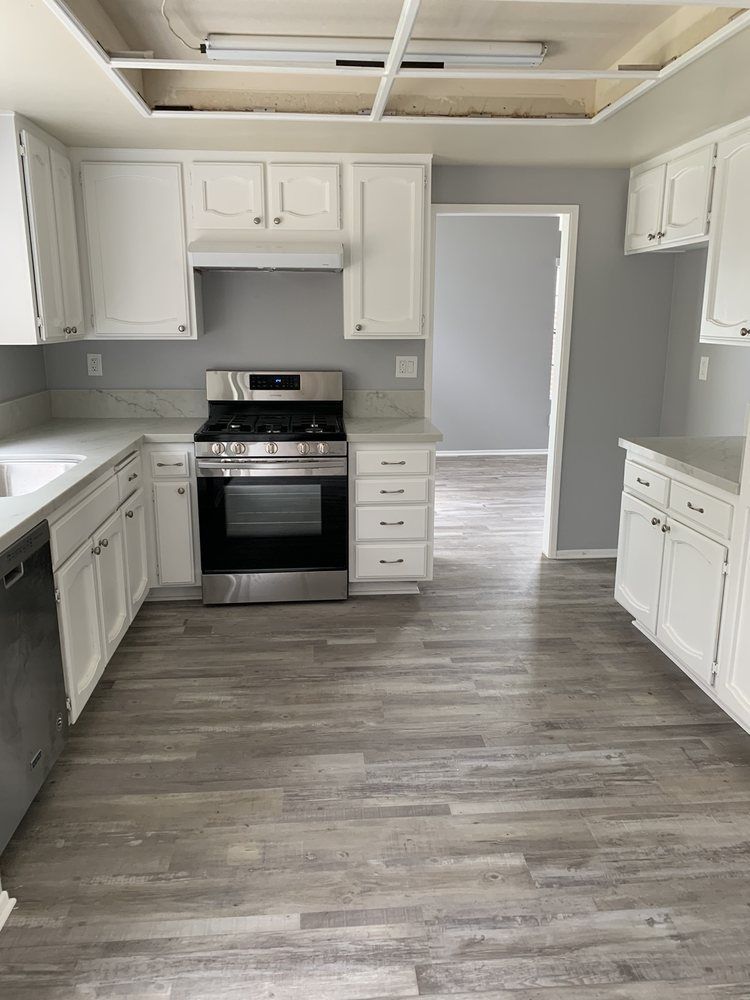 Empty white kitchen with gray wood-look floors, white cabinets, and stainless steel stove.