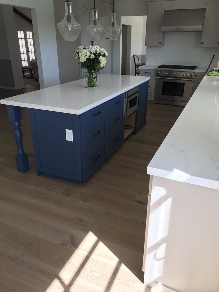 Modern kitchen with blue island, white countertops, and vase of flowers on wood floors.