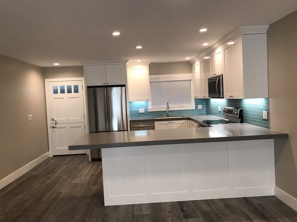 Bright modern kitchen with white cabinets, gray countertops, stainless fridge, and dark wood floors.
