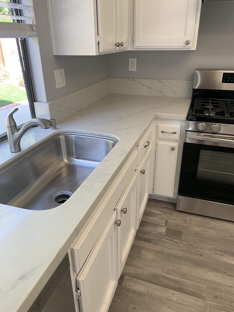 White kitchen with stainless sink, white cabinets, and stainless gas stove beside a marble-look countertop