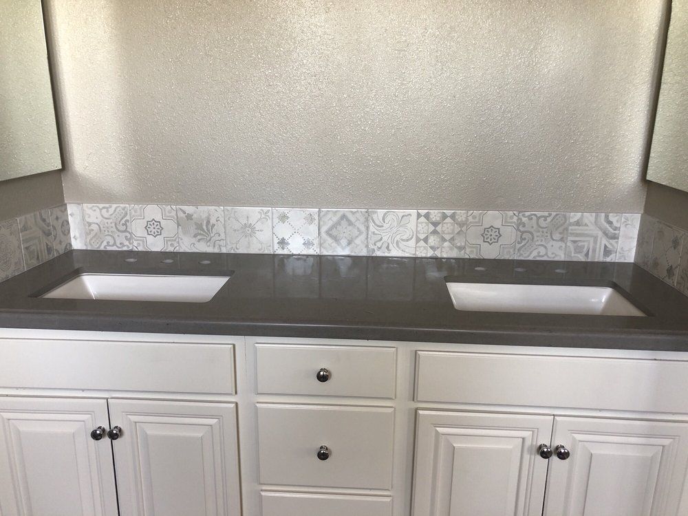 Double vanity with gray countertop, white cabinets, and two sinks against a patterned tile backsplash