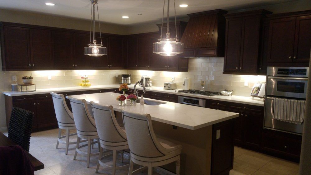 Modern kitchen with dark cabinets, white island, bar stools, and pendant lights
