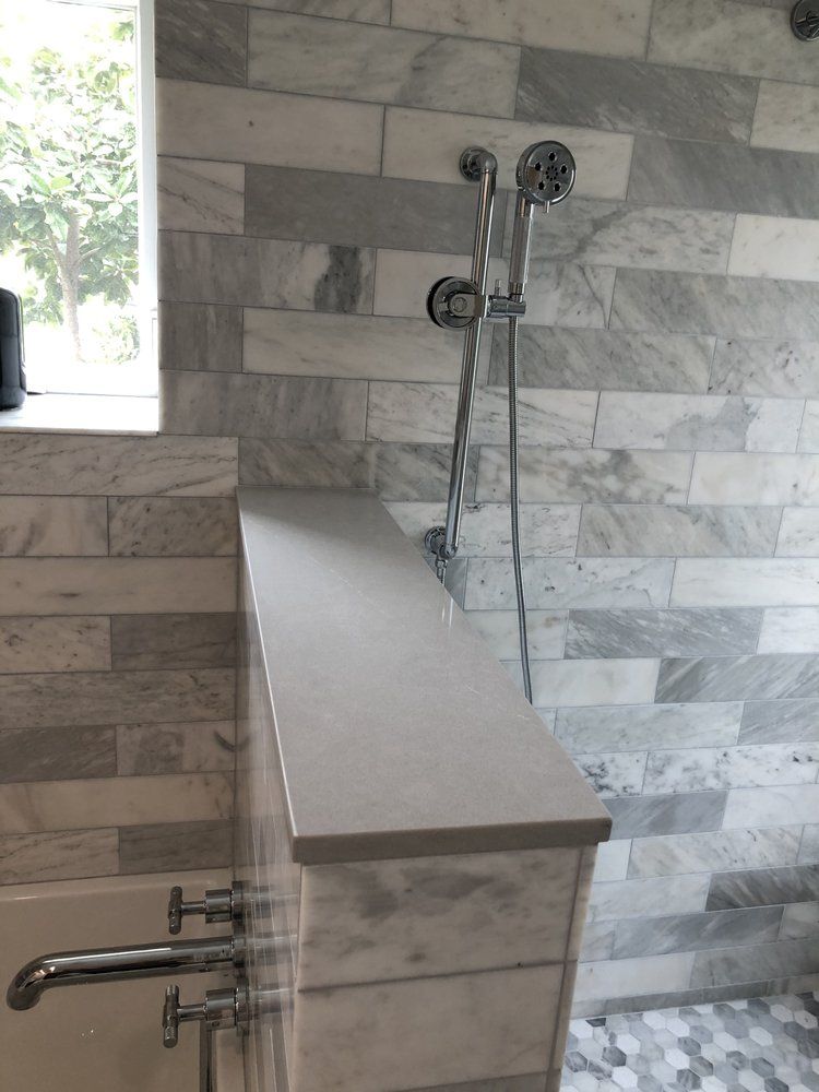 Shower stall with gray tile walls, built-in bench, and chrome shower fixtures.