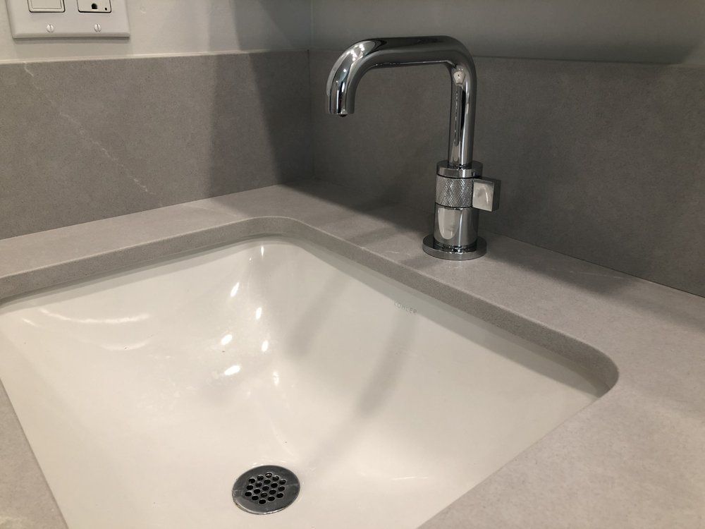 Modern white sink with chrome faucet set into a gray countertop and backsplash.