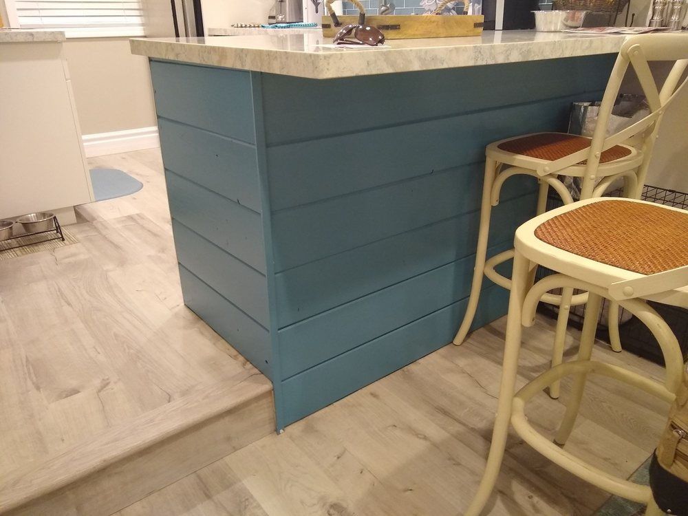 Teal kitchen island with marble countertop and wicker chairs on light wood flooring