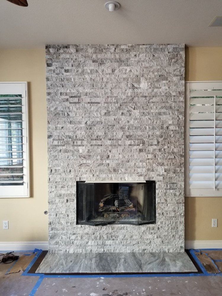 Stone fireplace wall with a black firebox in a beige living room, bordered by blue painter’s tape.