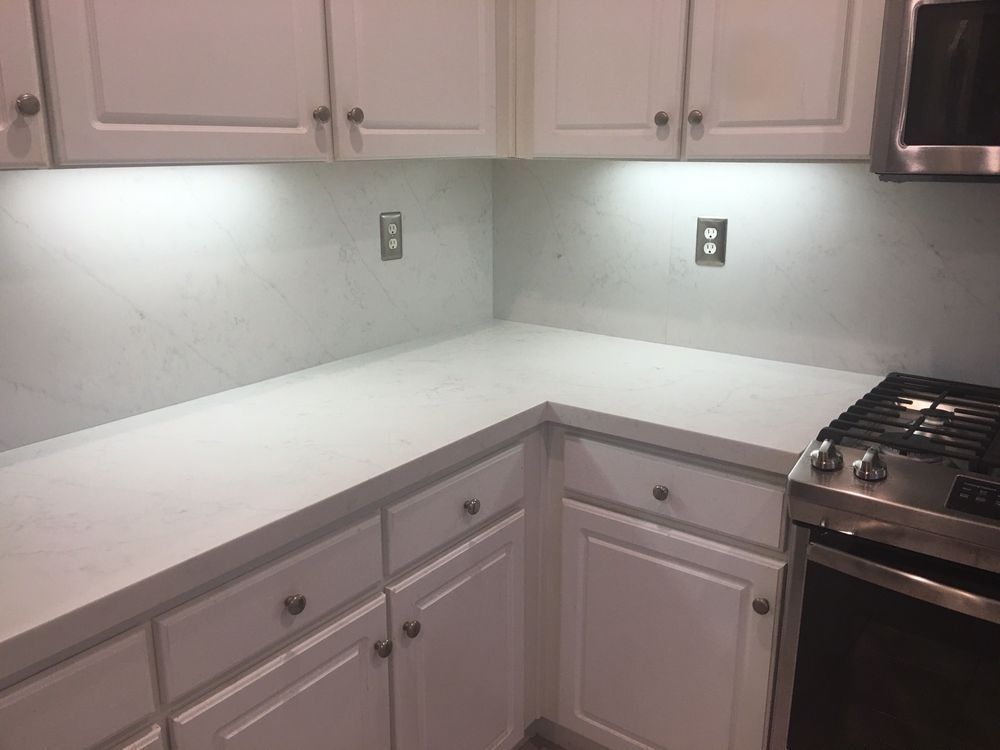 Empty kitchen corner with white countertops, light cabinets, and a stainless steel stove.