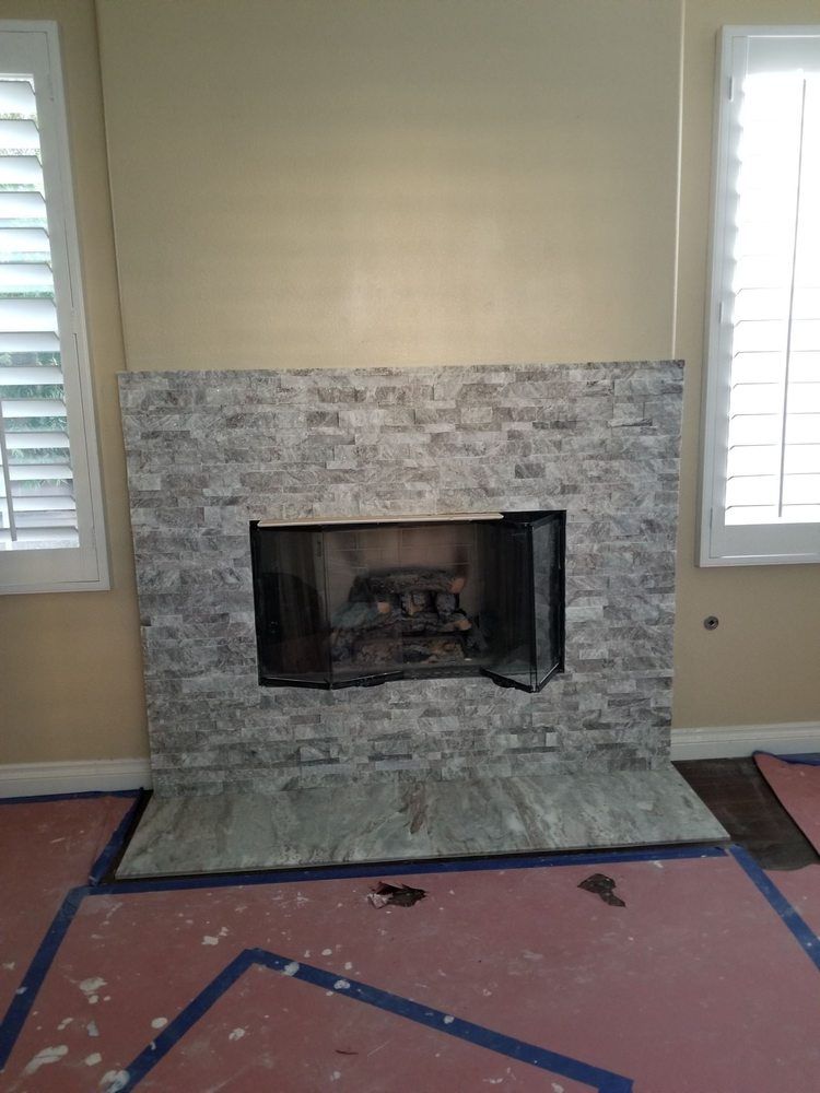 Living room fireplace with gray stone surround and white shutters on both sides, over pink carpet marked with blue tape