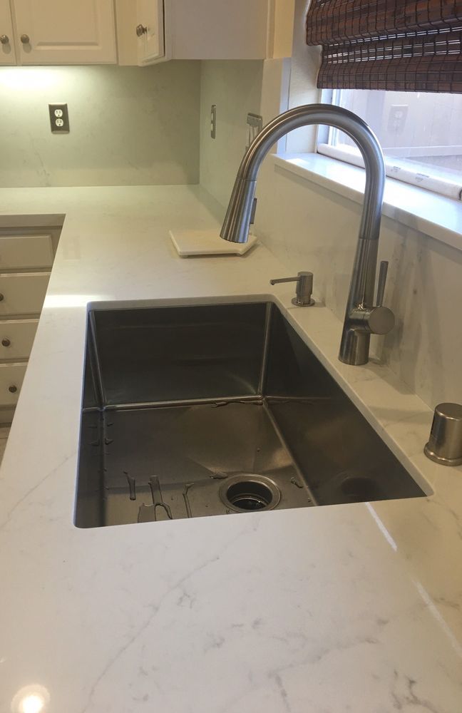 Modern kitchen sink with tall chrome faucet and white countertop by a window