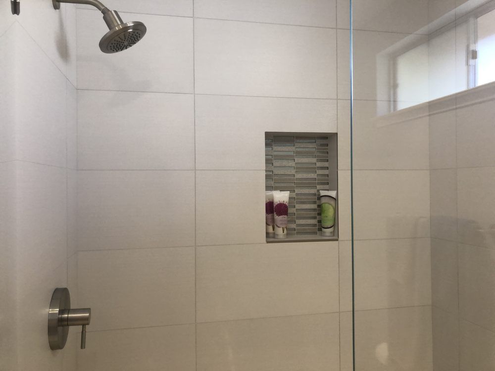 Modern tiled shower with glass door, chrome fixtures, and a recessed shelf holding toiletries.