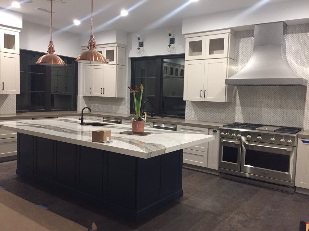 Modern kitchen with white cabinets, dark island, copper pendants, and stainless steel range and hood