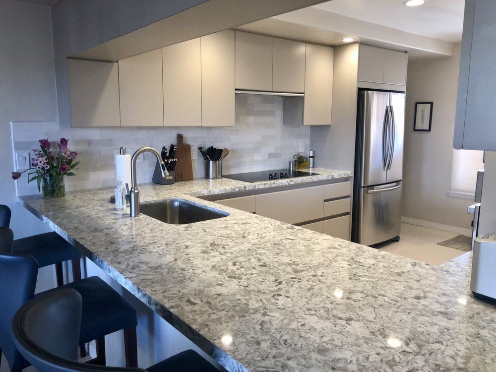 Modern kitchen with granite island, stainless steel appliances, and bar stools beside a dining area.