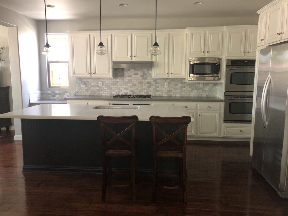 Modern white kitchen with island, two stools, stainless appliances, and dark wood floors
