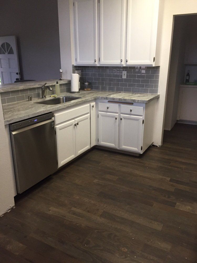 Kitchen with white cabinets, gray tile backsplash, stainless dishwasher, and dark wood floor.