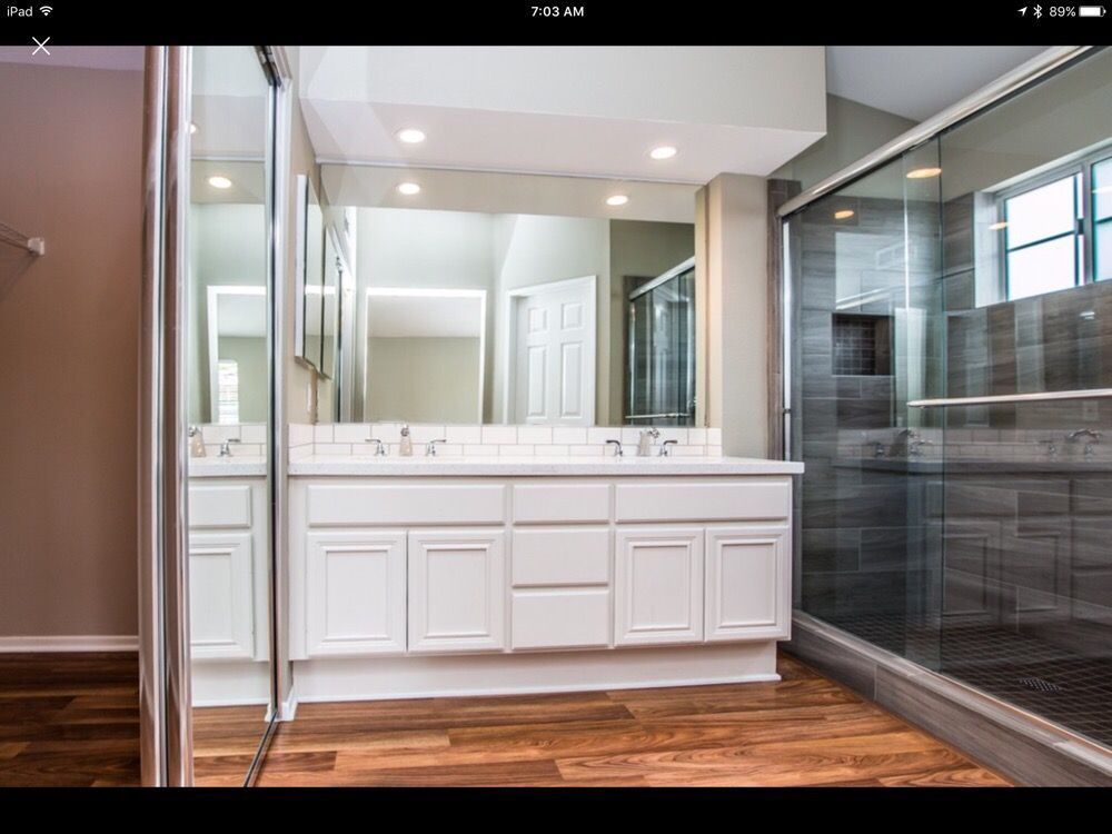 Luxury bathroom with white double vanity, large mirror, and glass-enclosed shower beside wood flooring